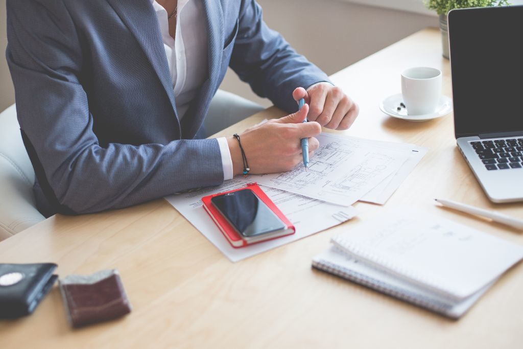 Sales person wearing blue blazer holding a pen with a contract and laptop on desk